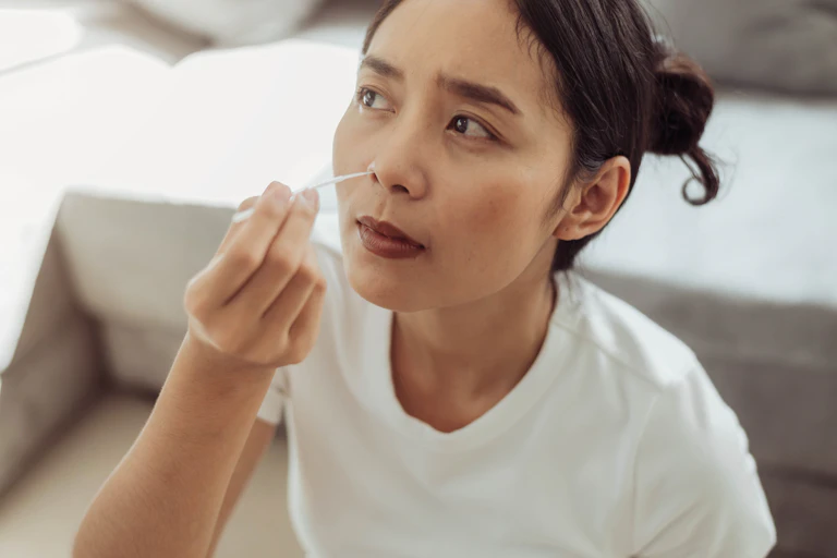 Woman inserts COVID home testing swab into her nose.