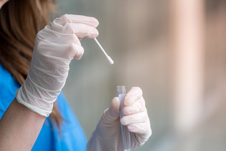 Nurse puts a swab into a tube.