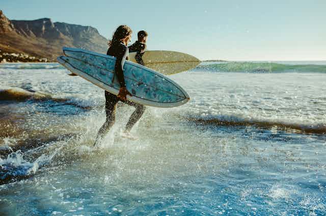 Two people running with surf boards into the ocean