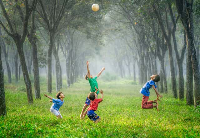 A group of boys play football in a forest setting. 