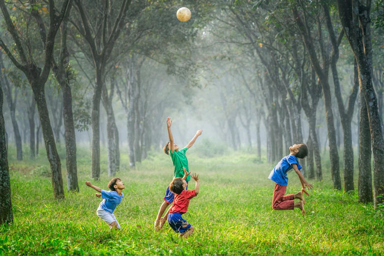 A group of boys play football in a forest setting.