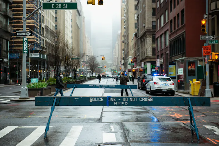 A police barrier blocks the entrance to a large avenue in New York City.