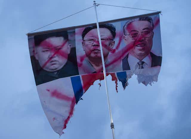 A banner showing the defaced photos of (L-R) North Korean leaders Kim Jong Un, Kim Jong Il, and Kim Il Sung.