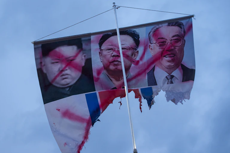 A banner showing the defaced photos of (L-R) North Korean leaders Kim Jong Un, Kim Jong Il, and Kim Il Sung.
