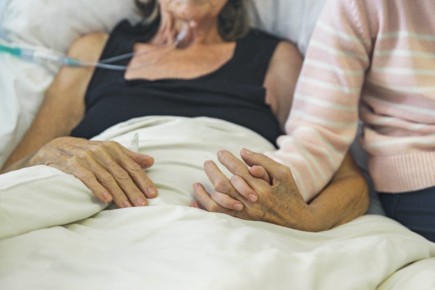 A dying woman is comforted by someone holding her hand.