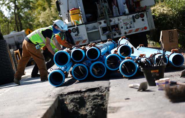 Utility worker stacks blue water pipes behind a truck.