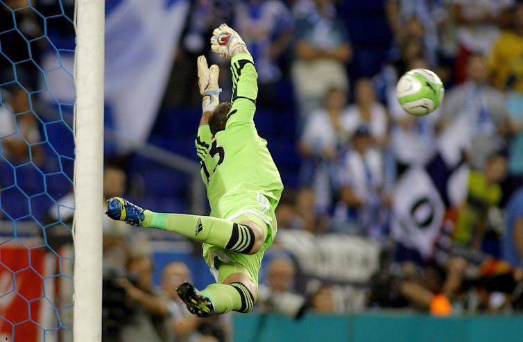 A goalie leaps through the air to block a football.