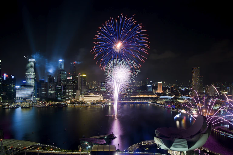 Fireworks exploding over a city harbor.