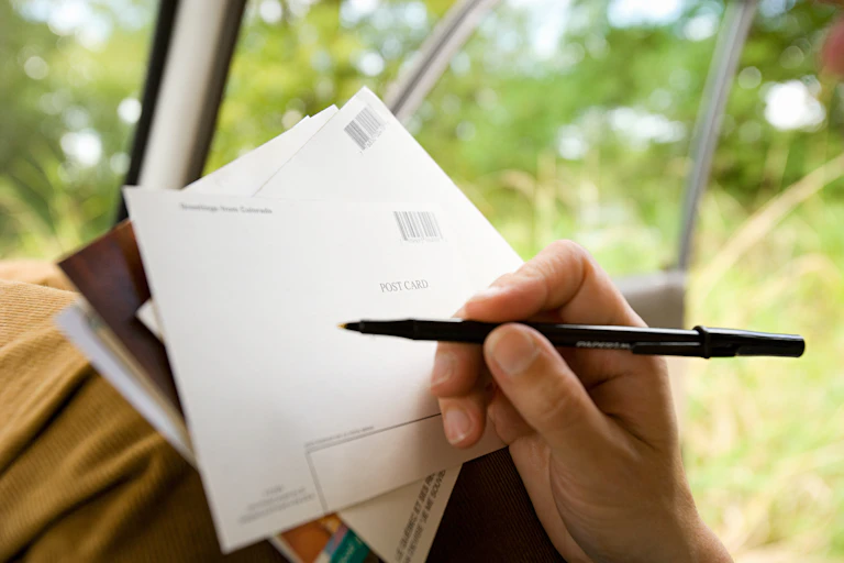 A hand holds a pen to a postcard