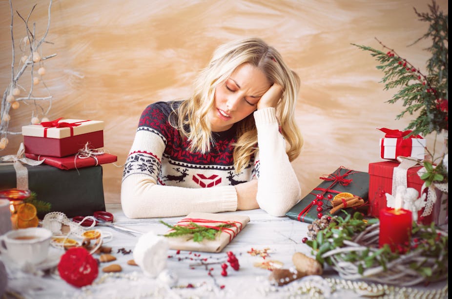 Stressed woman wearing a Christmas jumper takes a break from wrapping presents.