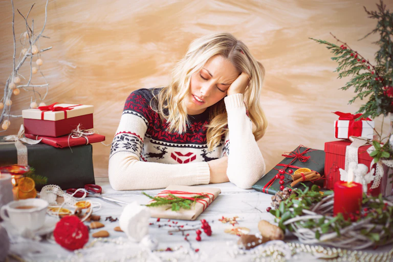 Stressed woman wearing a Christmas jumper takes a break from wrapping presents.