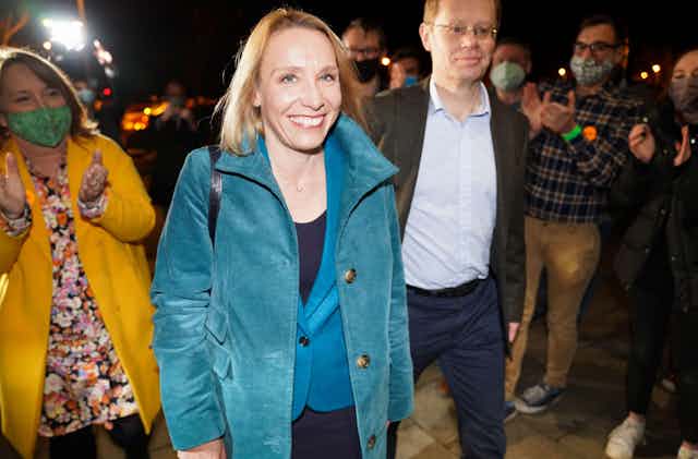 Helen Morgan wearing a bright blue blazer and coat, smiles as she arrives at the location of the election count