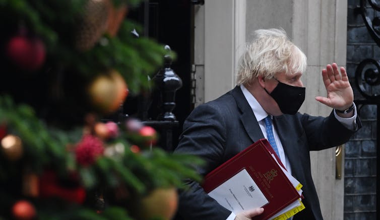 A masked Boris Johnson exits Downing Street, looking away from the camera and waves while looking away from the camera