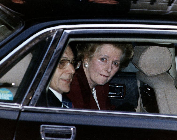 Margaret Thatcher parecendo chorosa na parte de trás de um carro.