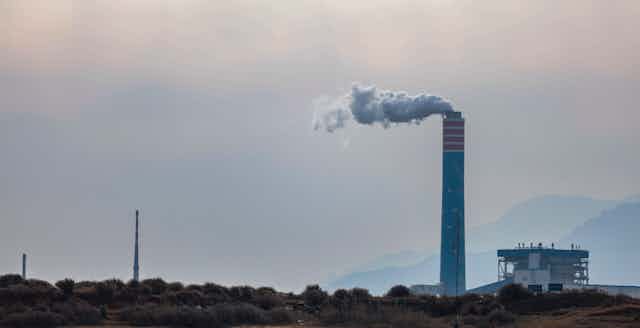 A single smokestack looms over a hill.