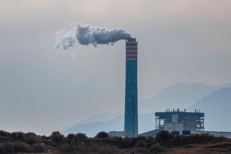 A single smokestack looms over a hill.