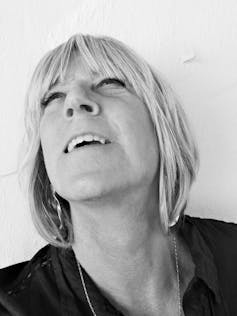 Black and white photo of a trans woman with medium length light hair looking up and smiling.