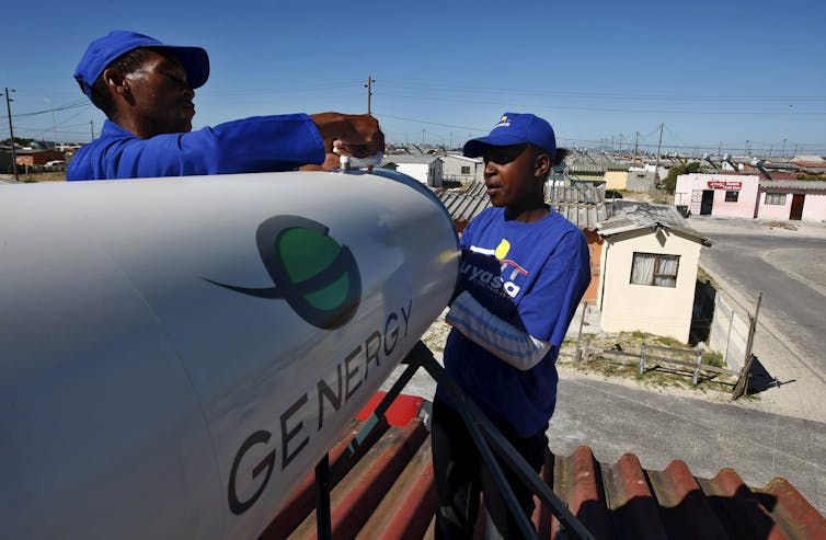 Engineers adjust a white, cylindrical tank on a roof.