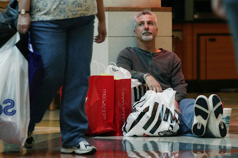 Man sits on mall floor surrounded by shopping bags.