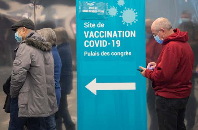 People in line at a vaccine site in front of a sign that points them to the clinic.