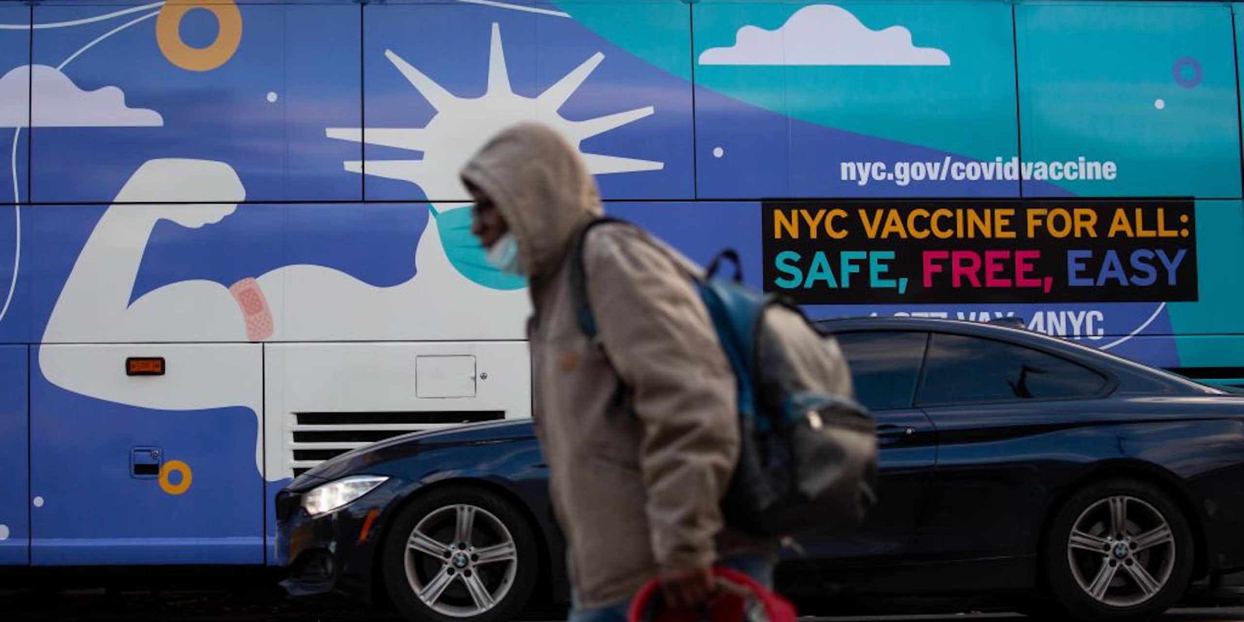 A pedestrian walks in front of a van with an ad that says "NYC VACCINE FOR ALL: SAFE, FREE, EASY"  