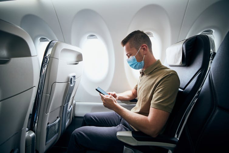 Man wearing face mask using mobile phone on a plane