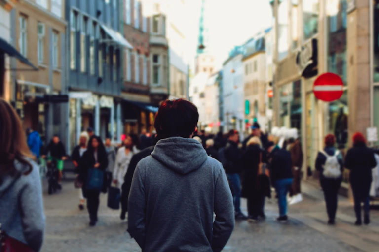 An isolated in a city looking at crowds of people.