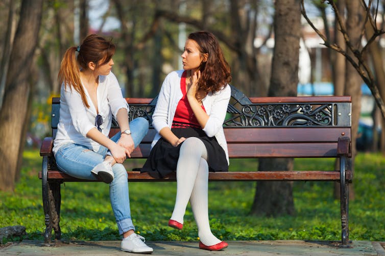 Two women talking on a bench in a park.