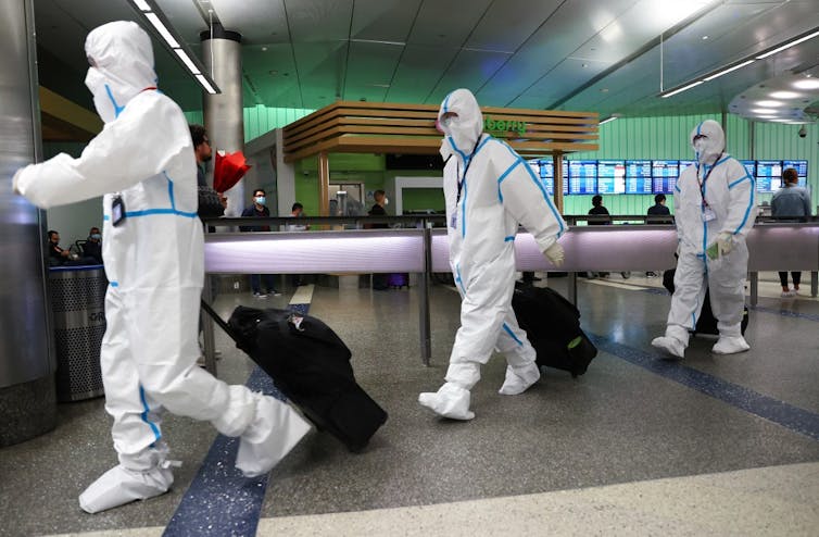 Trois voyageurs venant de Chine sortent d’un aéroport américain avec combinaison de protection de protection