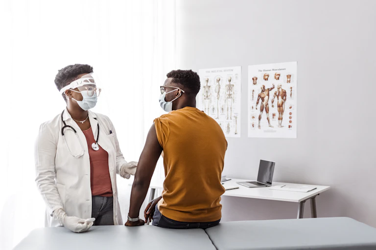 A female doctor wearing protective gear talks with a male patient prior to administering a vaccine.