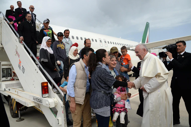 Pope Francis I welcomes Syrian refugees to Italy at the foot of an aircraft's steps.