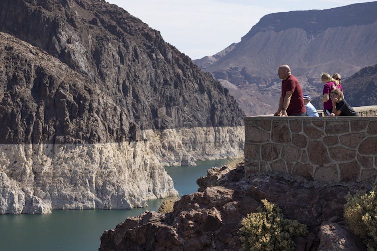 People looking from a viewing platform at Lake Mead, where a white ring on the stone walls shows how far water has dropped below normal.