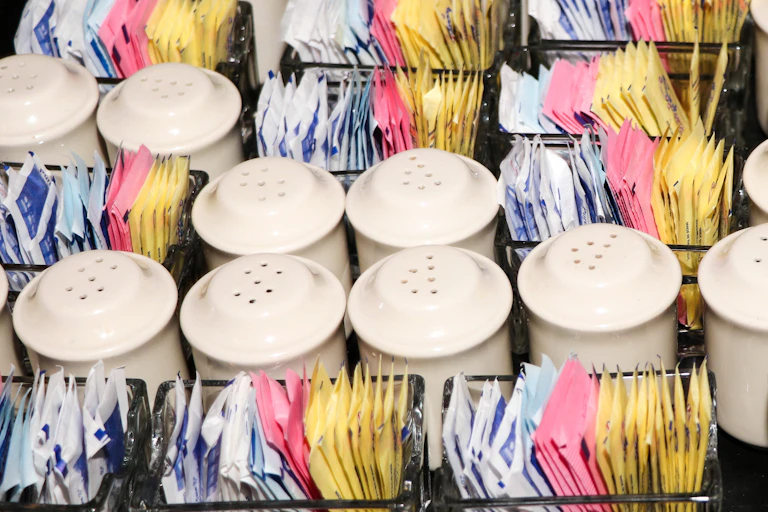 Many colored packets of sweetener and sugar shakers.