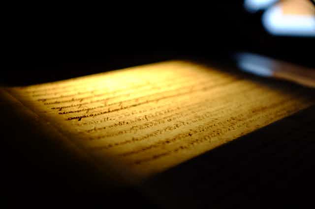 Feuille de papier couverte d'écriture, vue de coté, éclairée par une lumière jaune / dorée