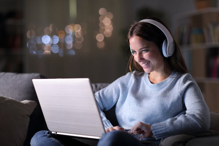 Woman wearing headphones smiles at laptop