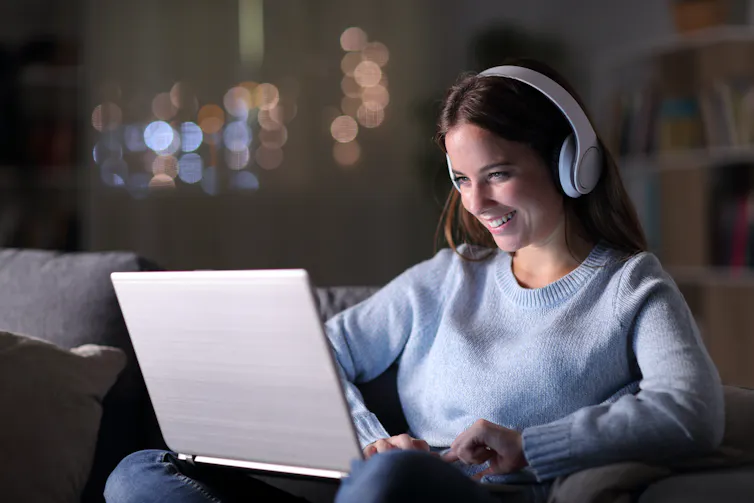 Woman wearing headphones smiles at laptop