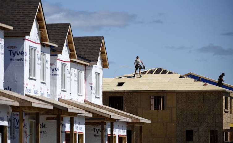 Construction worker standing on a half-finished roof. In the foreground there are three half-built houses.