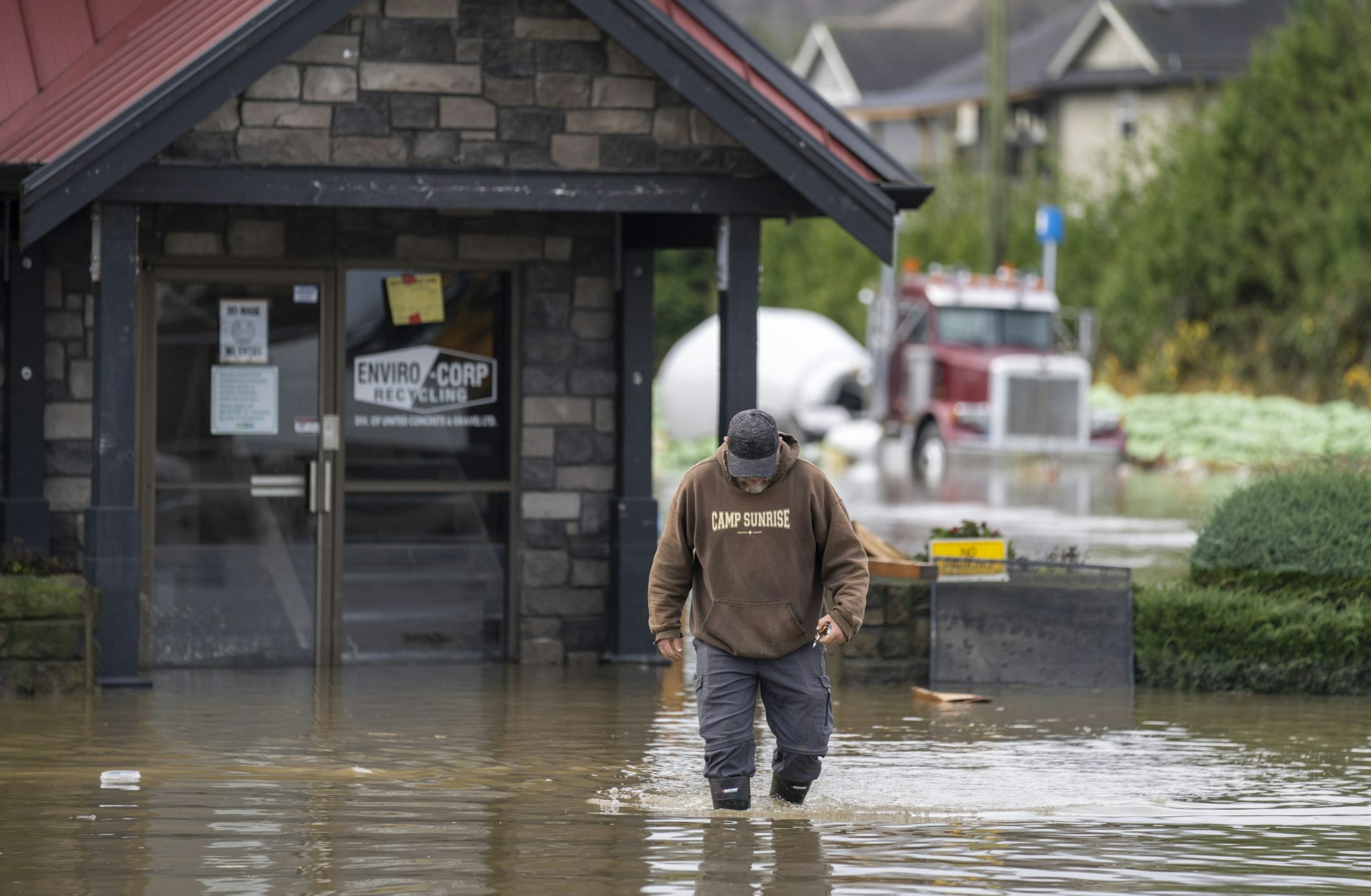 A man walking through knee-high water. In the background, a large truck and the front of a building are submerged in the water.