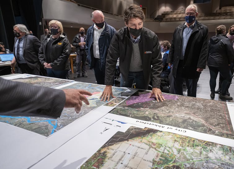 A group of men, all wearing face masks, examine a large map on a table