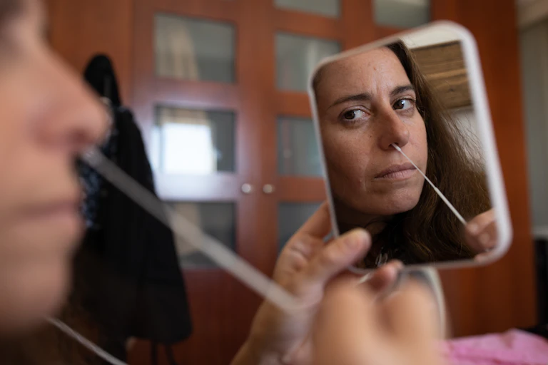 A woman holds a mirror as she conducts a nasal swab.