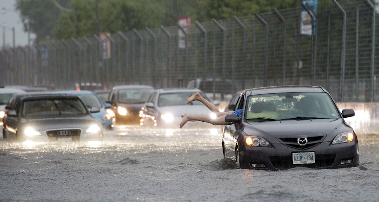 A pair of legs sticking out of a car sitting in the middle of a flooded highway
