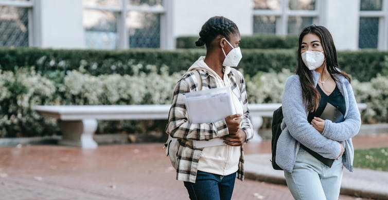 Two students seen wearing masks walking outside.
