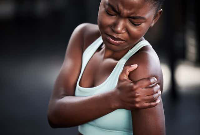 A woman holds her shoulder in pain.