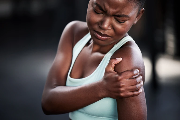 A woman holds her shoulder in pain.