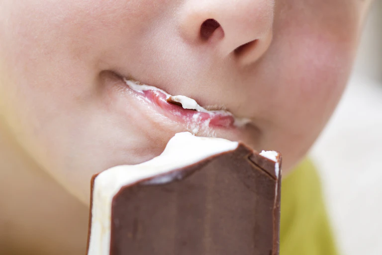 Close-up of nose and mouth of a kid eating an ice cream sandwich.