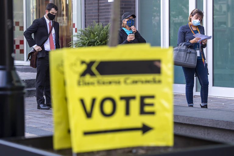 Three people wearing masks standing behind a "VOTE" sign.