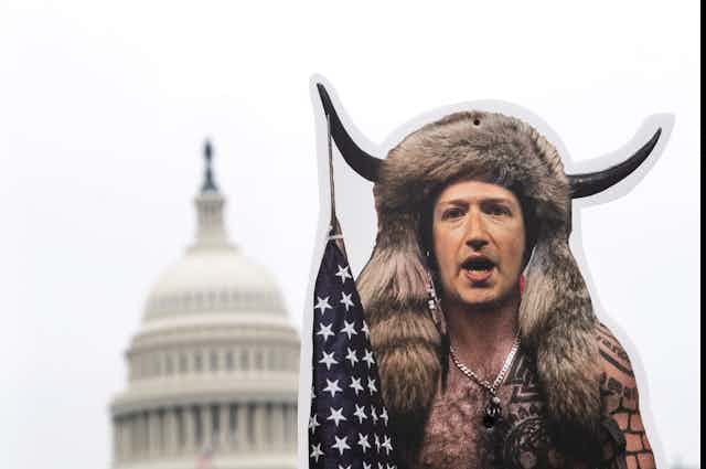 A cutout display of a man wearing a fur headdress with bison horns and holding a U.S. flag is positioned in front of the US Capitol building