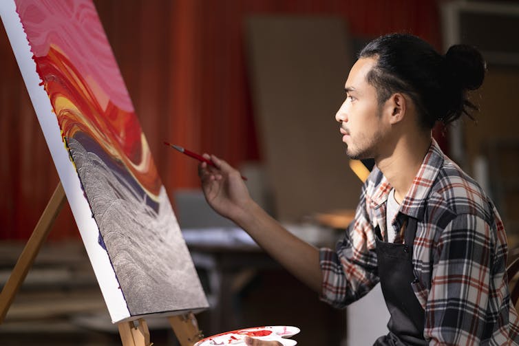 Un hombre pinta sobre lienzo en un estudio.