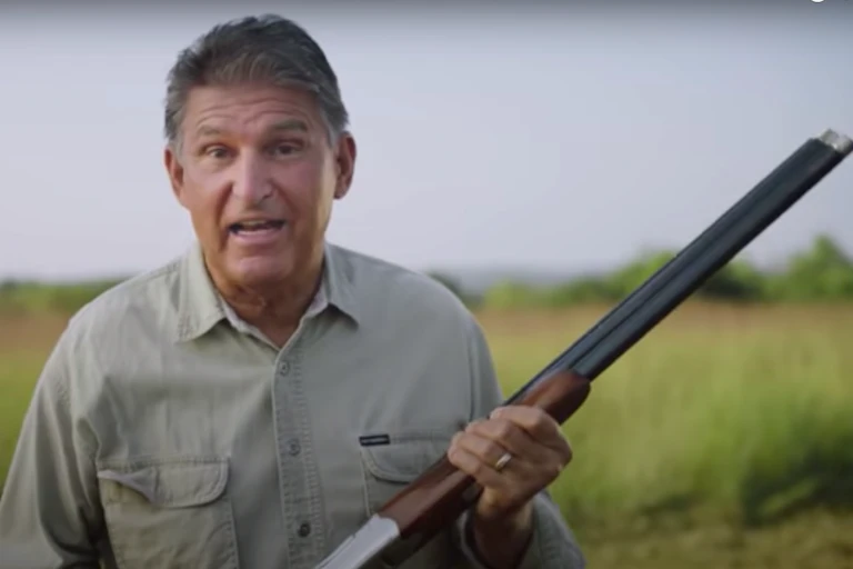 Senator Joe Manchin facing the camera holding a shotgun.