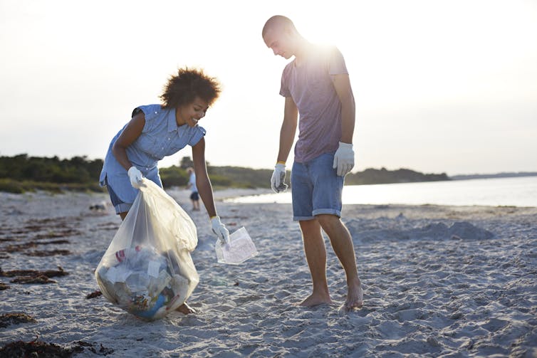 A man and woman pick up plastic waste on a beach.